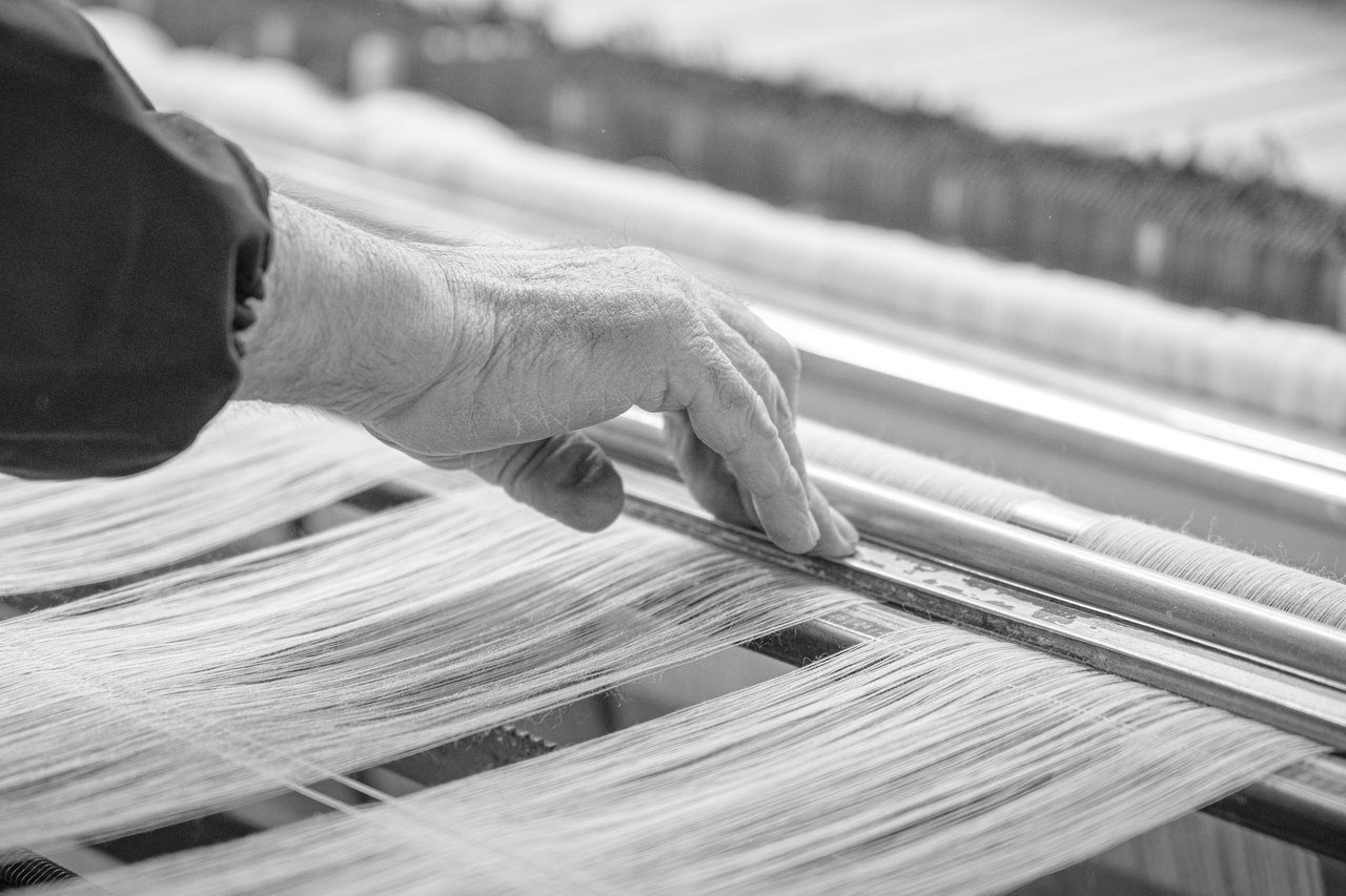 Le mani di un tessitore sui fili dell'ordito, al telaio