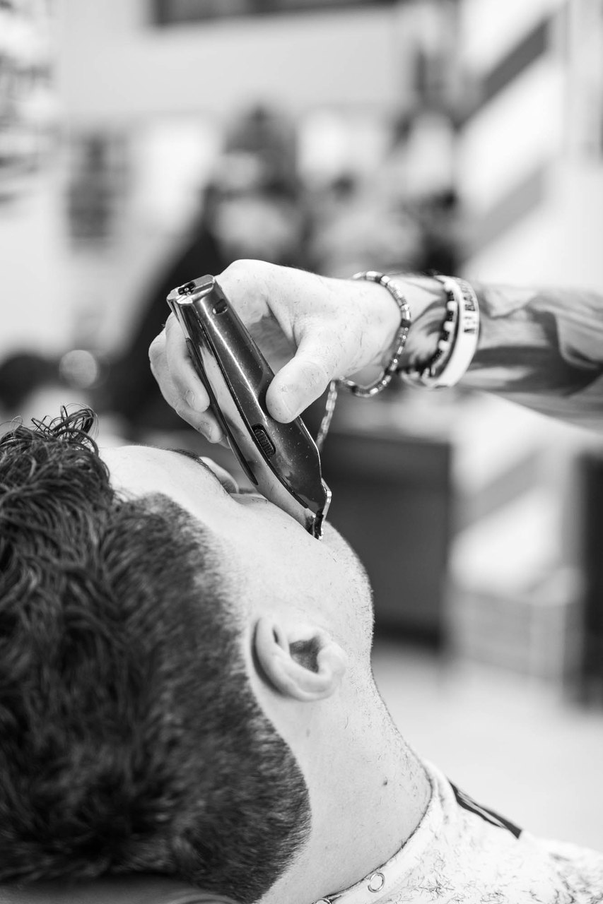 La macchinetta disegna il contorno della barba sotto il mento, il cliente con la testa all'indietro