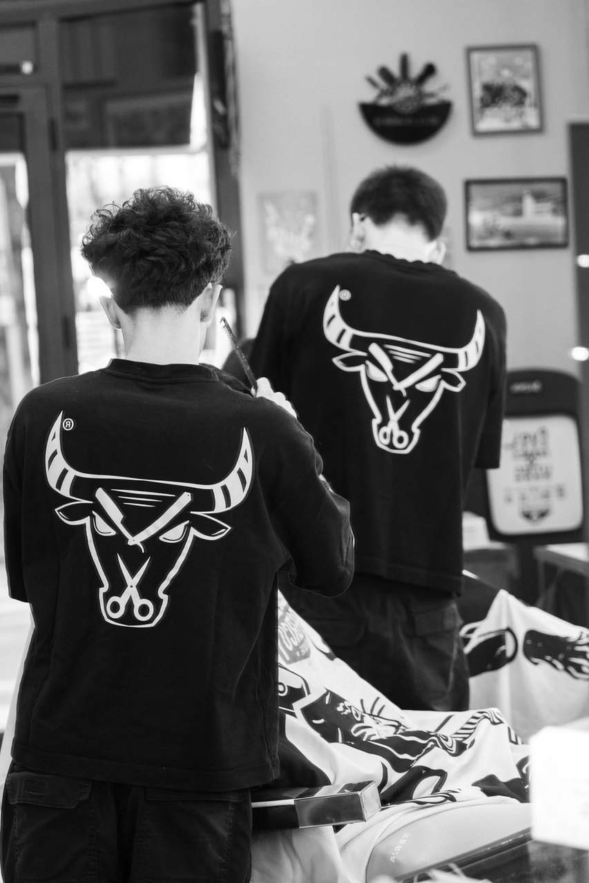Due barbieri di Bullbarber di spalle, il toro con le forbici stampato sulle maglie