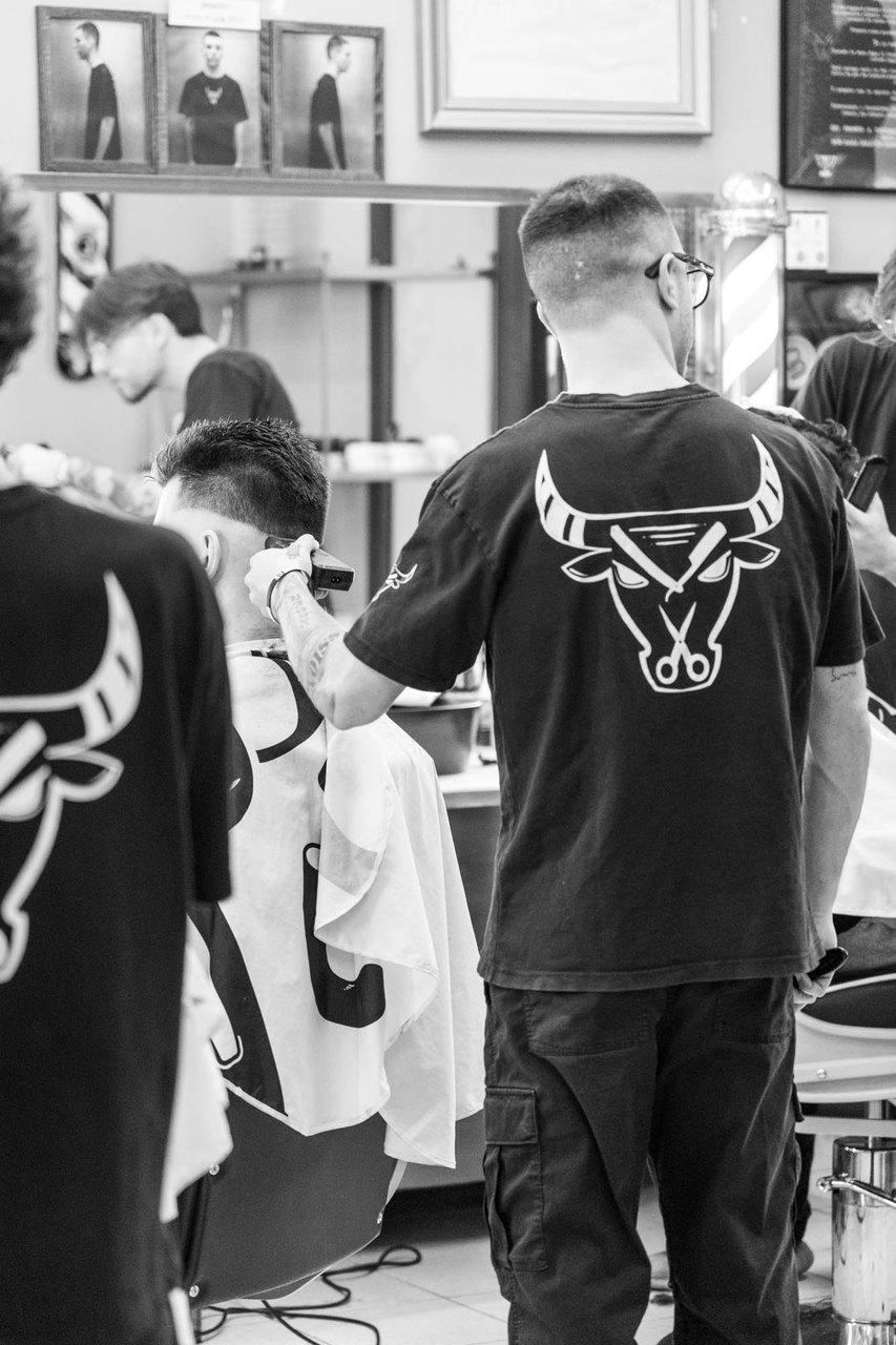 Un barbiere di spalle, col toro sulla maglia, passa la macchinetta sulla testa del cliente