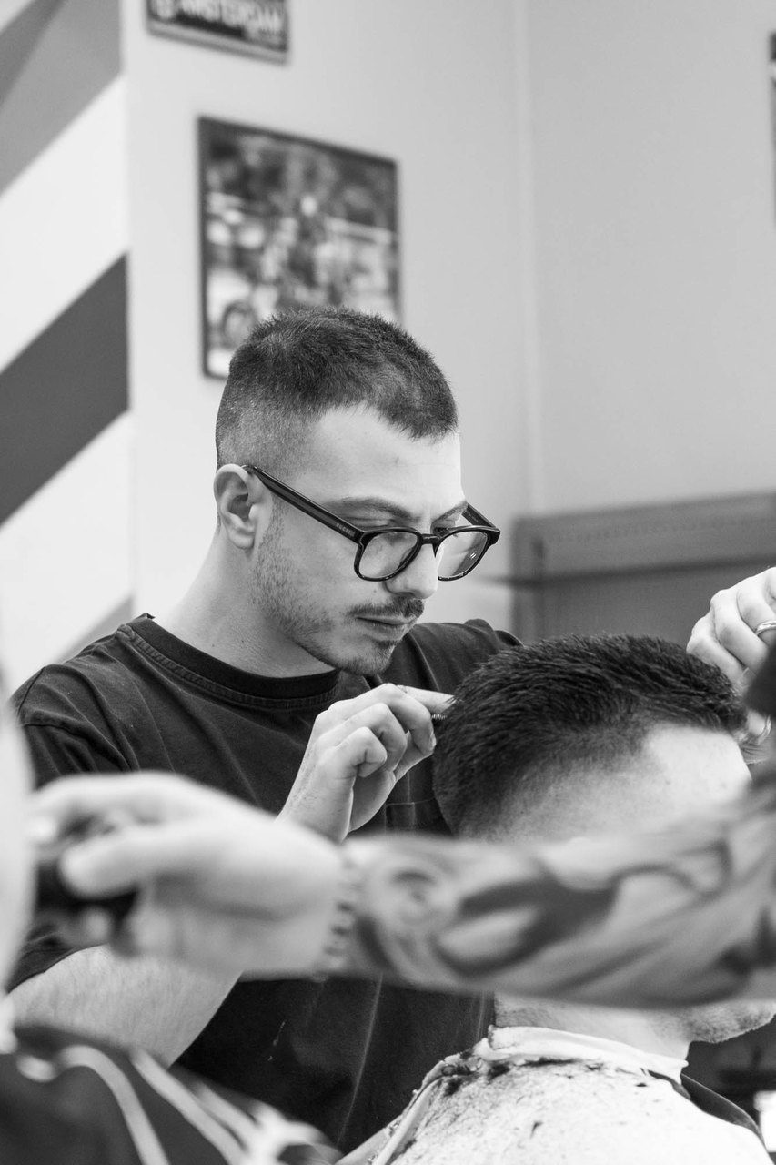 Un barbiere con gli occhiali rifinisce il taglio sopra l'orecchio di un cliente di spalle