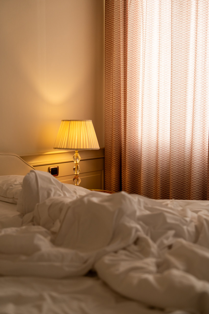 Una camera con la luce calda della lampada e il letto disfatto