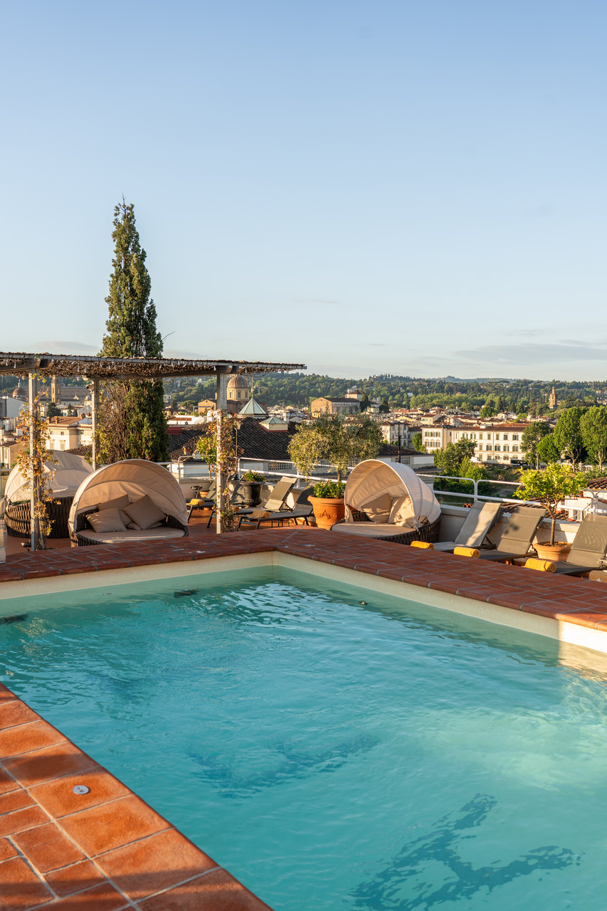 La piscina sul tetto dell'hotel coi lettini e i cipressi, di mattina