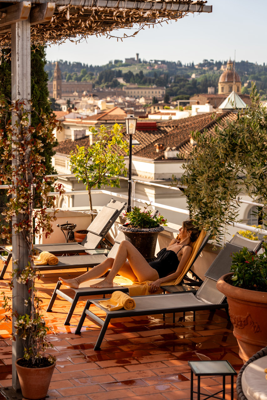 La terrazza della piscina fra le piante, con una ragazza sul lettino e i colli di Firenze