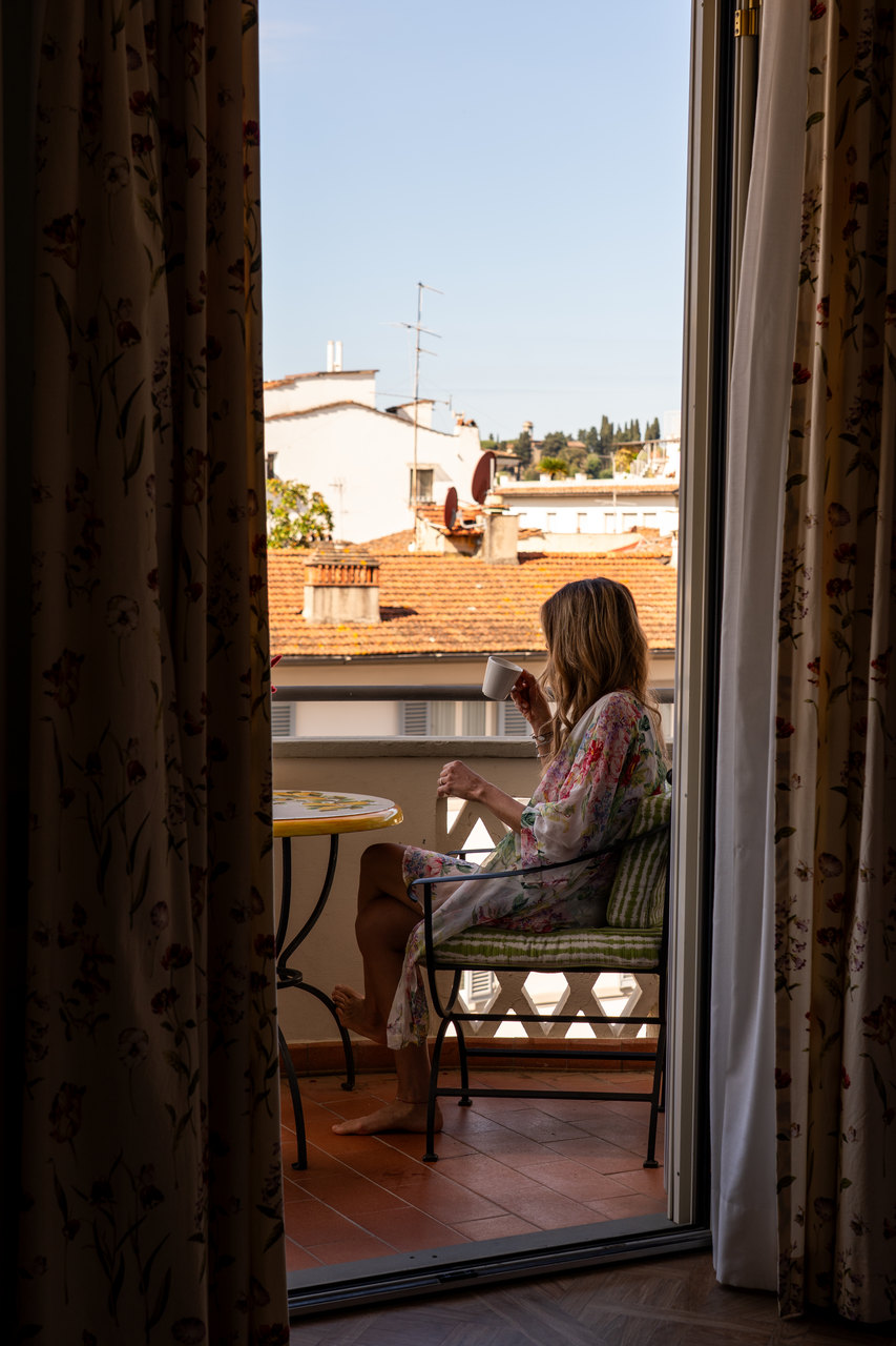 Una ragazza beve un caffè sul balcone di una camera, vista dalla stanza