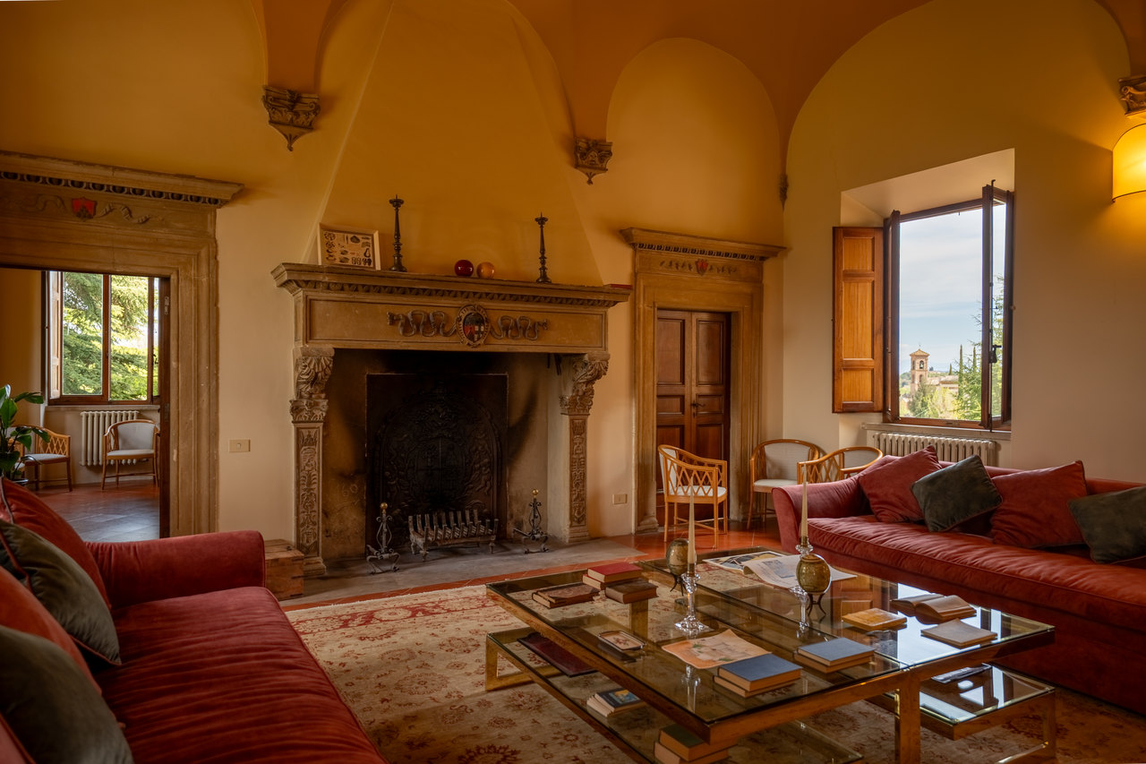 Il salone col grande camino di pietra, i divani rossi, il tavolo basso e le finestre aperte sul giardino