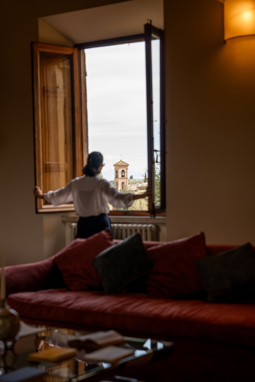 Una donna di spalle apre la finestra di una sala sul campanile e sulla campagna