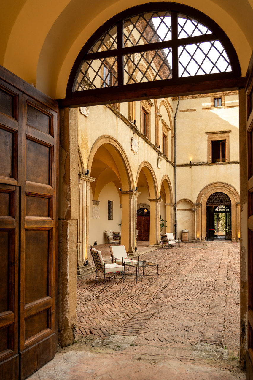 Il cortile visto dal portone d'ingresso: gli archi su due piani, il portale di pietra, il cotto a spina di pesce e le poltroncine