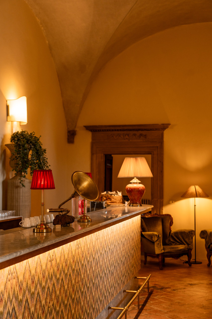 Il bar sotto la volta: il bancone illuminato a motivo fiammato, la lampada rossa, il grammofono e le poltrone di velluto