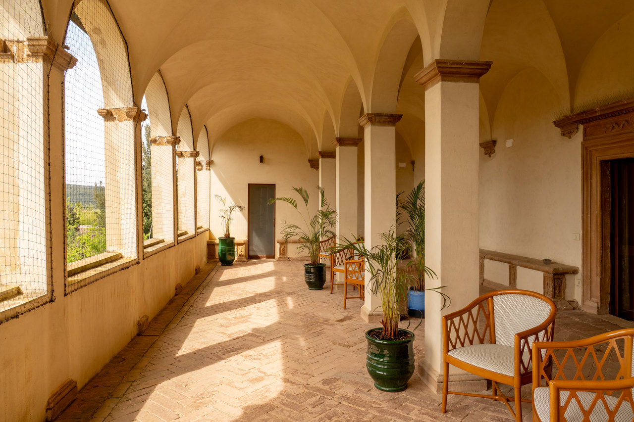 La loggia al primo piano di giorno: gli archi aperti sulla campagna, il cotto a spina di pesce, le poltroncine e le palme nei vasi