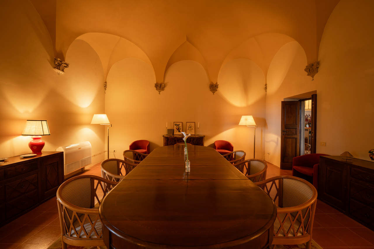 La sala col tavolo lungo ovale e le sedie, sotto le lunette, con le lampade rosse accese