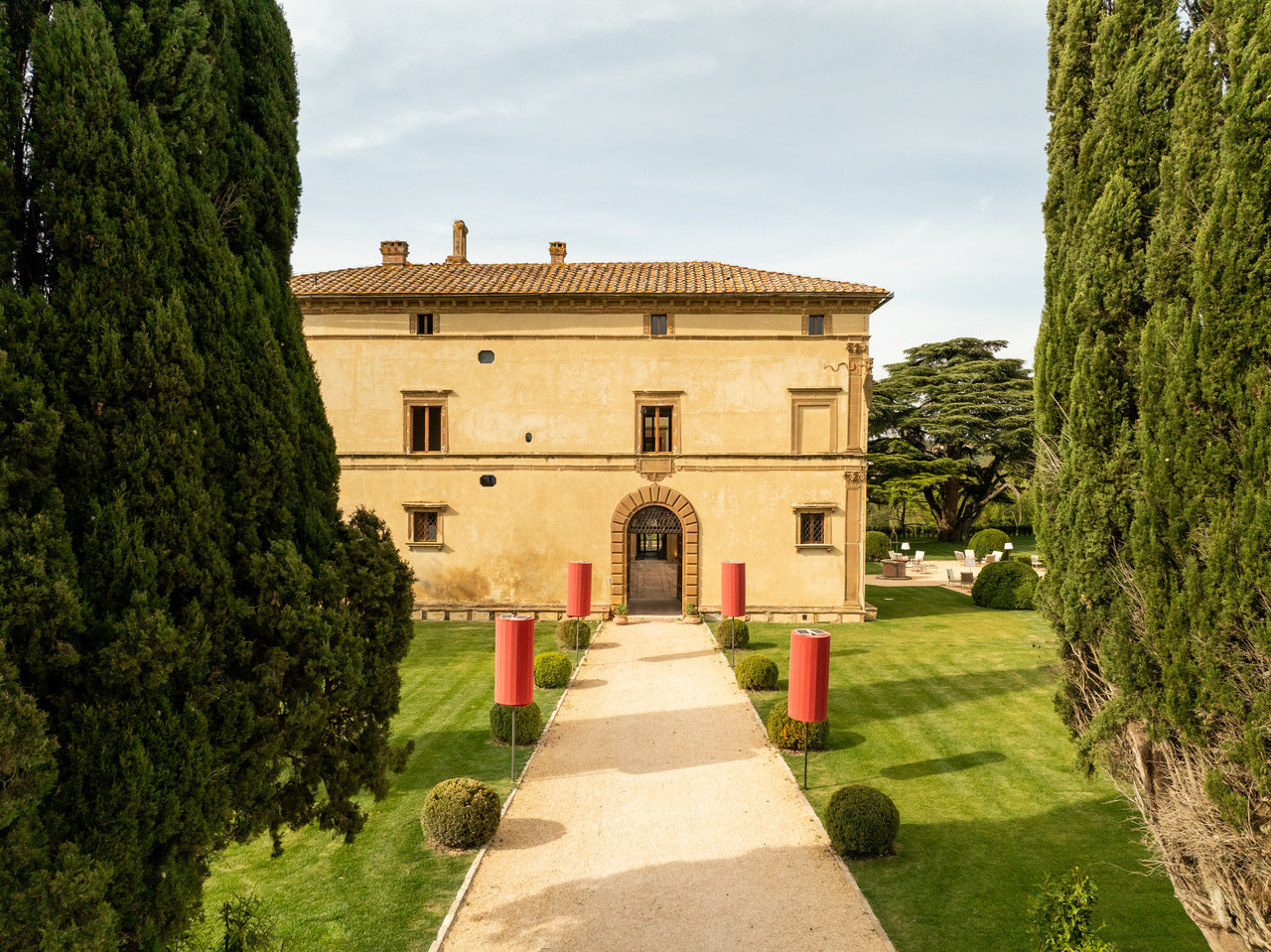 Il viale d'ingresso fra i cipressi visto dal drone, con le lanterne rosse e la facciata col portale di pietra, di giorno