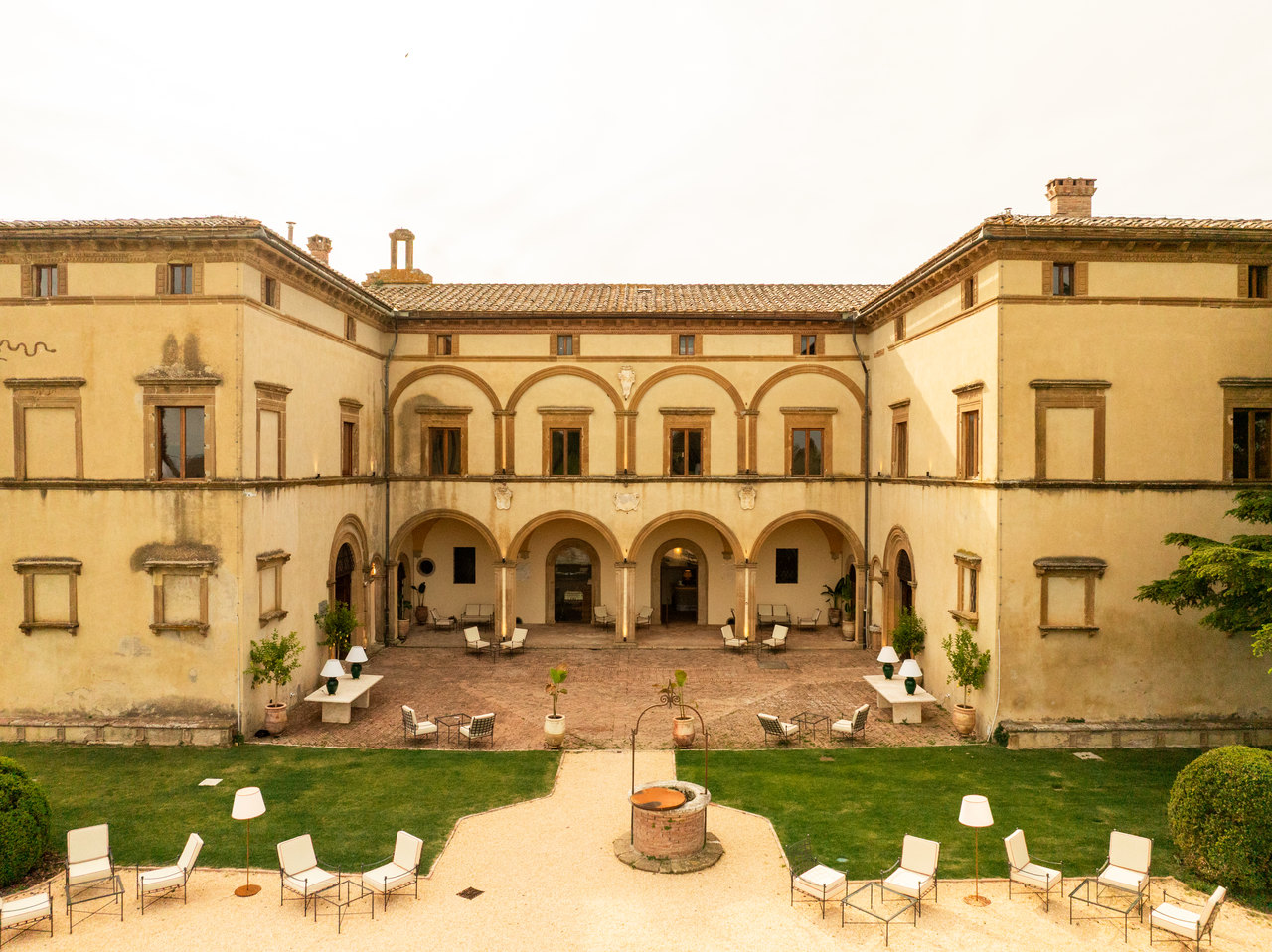Il cortile con gli archi su due piani visto dal drone, di giorno: il pozzo, la ghiaia, le poltroncine bianche e le lampade
