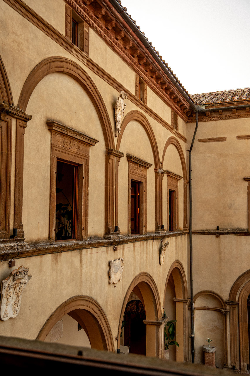 Il cortile dall'alto: gli archi su due piani, le finestre e gli stemmi nella luce del tramonto
